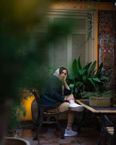 a woman sitting at a table in front of a potted plant with her hand on her chin