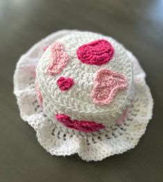 a crocheted white and pink hat with hearts on the top sitting on a table