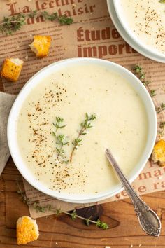 two white bowls filled with soup and garnished with herbs, on top of a wooden table