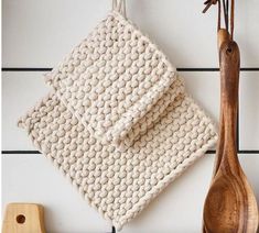 two wooden spoons and a white knitted dishcloth hanging on a wall next to a cutting board