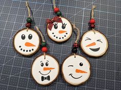 four snowman ornaments are hanging on wood slices