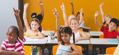 children sitting at desks with their hands in the air