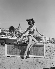 a woman in a bathing suit is jumping on the beach with her arms outstretched and legs spread out