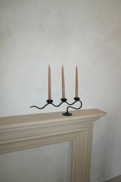 three candles are placed on top of a mantel in front of a white wall