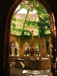 an archway leading into a courtyard with a fountain in the center and trees on either side