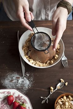 a person scooping ice cream out of a bowl with strawberries on the side