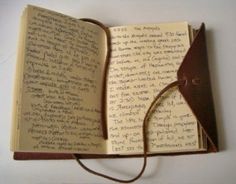 an open book with writing on it and a brown leather strap hanging from the cover