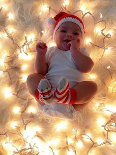 a baby is sitting in front of some christmas lights and wearing red and white socks