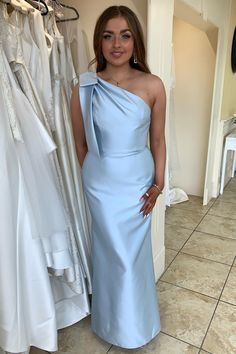 a woman in a blue dress standing next to some wedding gowns on hangers