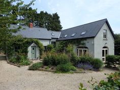 the house is surrounded by greenery and flowers on either side of the driveway area