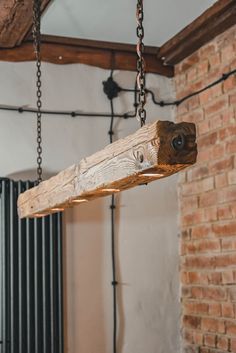 a wooden light fixture hanging from a beam in a room with brick walls and exposed beams