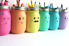 a row of colorful painted mason jars with faces on them and pencils sticking out of the lids