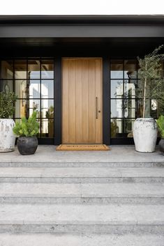 two planters on the steps in front of a house with wooden door and glass windows