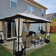 a patio covered with curtains and furniture in front of a house