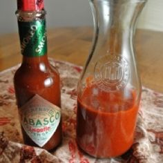 two bottles of hot sauce sitting on top of a cloth covered tablecloth next to each other