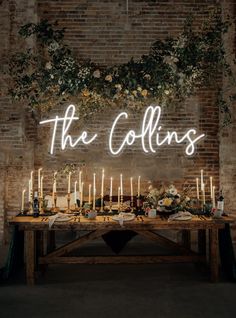 a table topped with candles and flowers under a neon sign that says the collinss