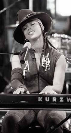 a woman wearing a brown hat sitting in front of a keyboard with a microphone behind her