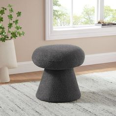 a grey stool sitting on top of a white rug next to a potted plant