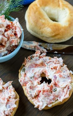 two bagels with crab salad on them next to a bowl of bread and knife