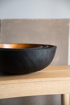 a black bowl sitting on top of a wooden table next to a brown chair with a white wall in the background