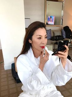 a woman in white robe brushing her teeth with an electric toothbrush while sitting on the floor