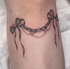 a woman's leg with a chain and bow tattoos on it