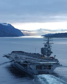 an aircraft carrier in the water with mountains in the background