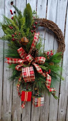 a christmas wreath hanging on the side of a wooden fence with pine cones and red plaid ribbon