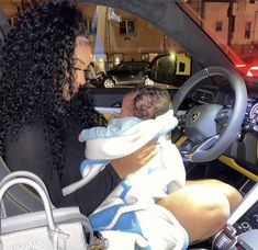 a woman holding a baby in her lap while sitting in the driver's seat of a car