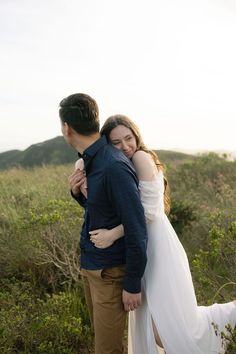 a man and woman standing next to each other in front of some bushes on a hill