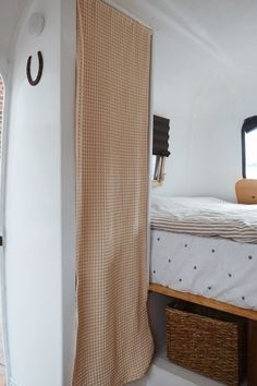 a bed sitting next to a window in a white room with a curtain hanging from it's side