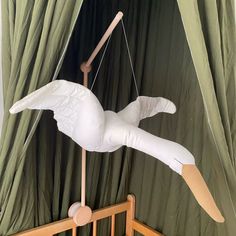 a wooden crib with a stuffed bird hanging from it's side and a green curtain behind it