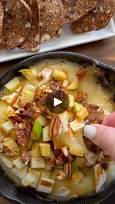 someone is holding their finger up to a bowl of food with bread in the background