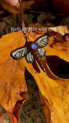 a person holding onto a leaf with a dragonfly on it's back and the words, hand sculpted with love