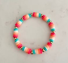 a bracelet with multi colored beads and gold accents on a white surface, top view