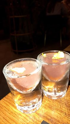 two glasses filled with liquid sitting on top of a wooden table next to each other