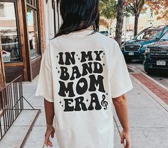 a woman walking down the street wearing a shirt that says in my band mom era