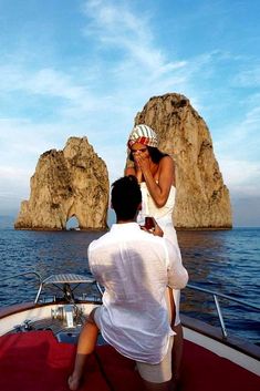 a man and woman sitting on the back of a boat in front of two rock formations