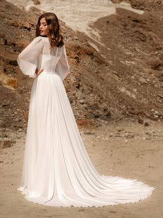 a woman in a white wedding dress standing on the beach with her back to the camera