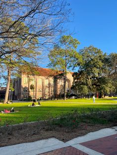 people are sitting on the grass in front of a large building with trees and flowers