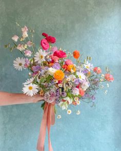 a person holding a bouquet of flowers with pink ribbon around the bottom and white daisies on top