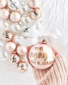 a hand holding a pink ornament with white ribbon and some ornaments around it