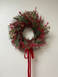 a wreath with red berries and green leaves hanging on a wall next to a ribbon