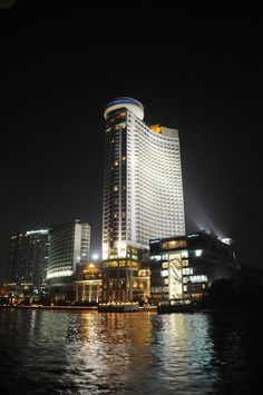 a very tall building sitting on top of a river next to a city at night