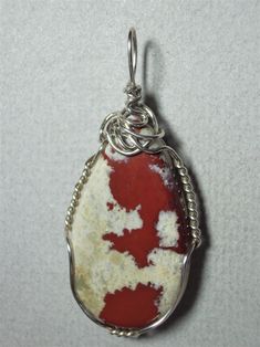 Pigeon Blood Jasper Cabochon Pendant Wire Wrapped in .925 Sterling Silver Round Wire This vividly contrasting stone cabochon provides red mottling within a white to cream-beige background. Best with red, white, pink, and green, but also quite versatile and makes an attractive appearance against most colors. Mottled pattern and non-standard shape give more appeal to an artistic view than that of a purist; standard shape and flat face contour, however, may appeal to a purist view. Description: A r White Agate Cabochon Jewelry, Red Oval Agate Jewelry, Artisan Jasper Jewelry In Oval Shape, Artisan Oval Jasper Jewelry, Untreated Red Sterling Silver Jewelry, Artisan Red Oval Jewelry, Unique Red Jewelry With Large Stone, Artisan Wire Wrapped Red Jewelry, Artisan Red Wire Wrapped Jewelry