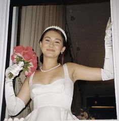 a woman in a white dress holding a bouquet of flowers and posing for the camera