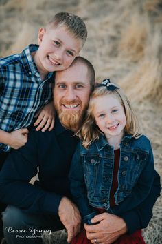 a man and two children are sitting on the ground in front of some dry grass