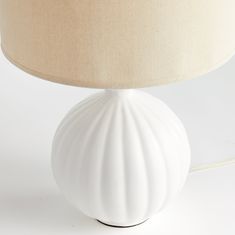 a white table lamp with a beige shade on the base and a light bulb attached to it