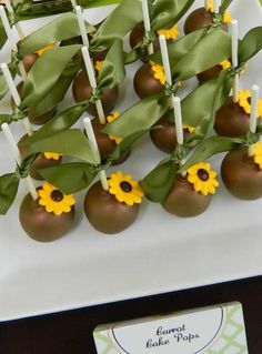 cake pops with sunflowers and green leaves are on a white plate next to a card