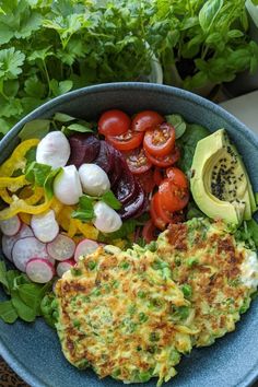 a blue bowl filled with vegetables and some sort of omelet next to an avocado